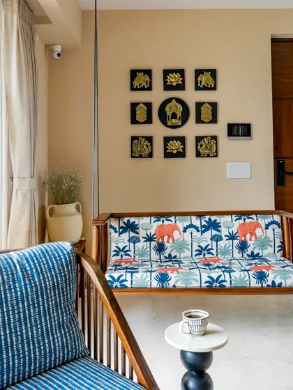 Another angle of the beautiful wooden swing, set against a beige wall with a curated gallery of traditional brass art, perfectly blending modern and ethnic design sensibilities.