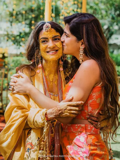 A sweet moment as a friend gives the haldi-covered bride a kiss on the cheek.