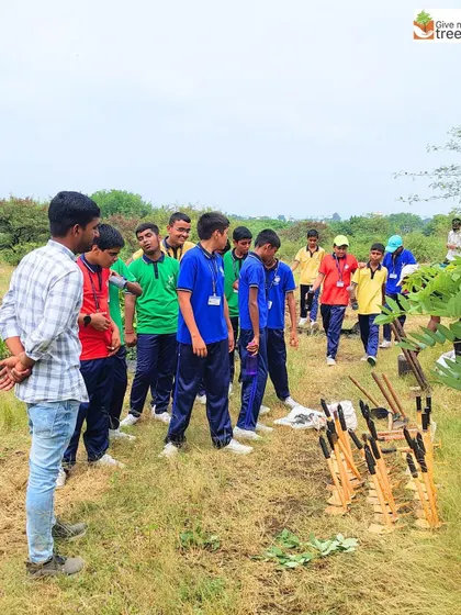 An instructor explains the planting process to a group of students, showing them the tools and saplings before they begin.