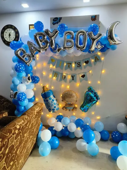 A lively 'It's a Boy' decoration for a home celebration. The setup includes a blue and white balloon arch, fairy lights, and multiple themed foil balloons.