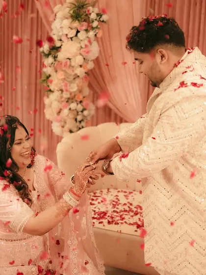 The couple celebrates their engagement, hands clasped, amidst a shower of red rose petals.