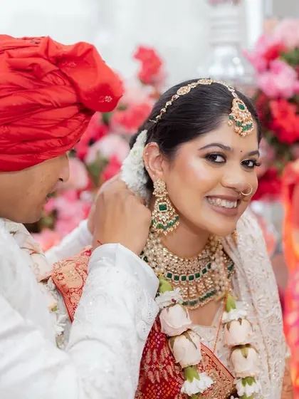 A close-up of the bride's radiant smile as the groom adjusts her jewellery. This intimate moment, with a family member looking on, is a beautiful example of the candid memories we capture.