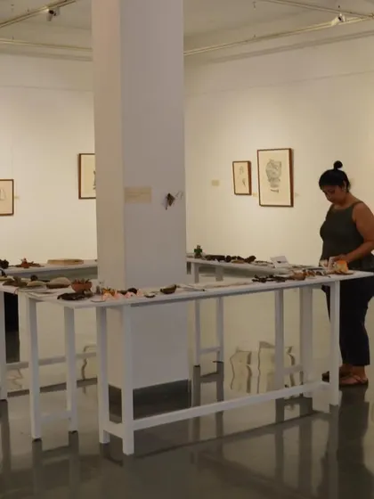 A visitor browses the long tables of found objects and small artworks at the 'Bring me Flowers' exhibition.