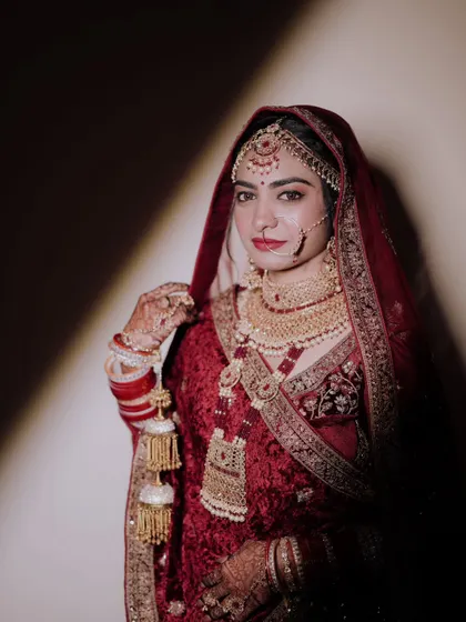 A dramatic bridal portrait using shadow and light to create a sense of elegance and mystery. The bride's direct gaze and stunning red lehenga make for a powerful image.