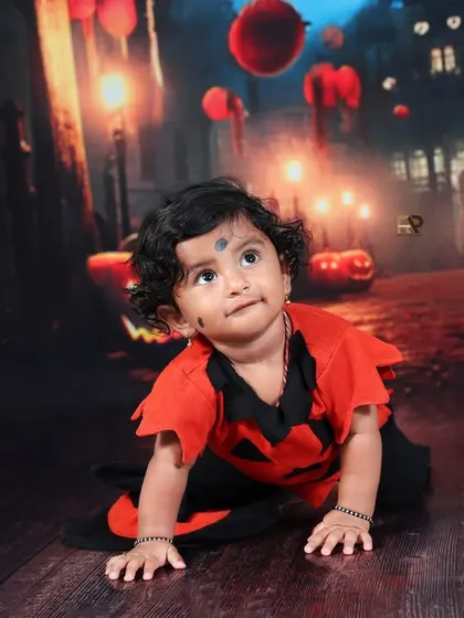 A crawling baby in a Halloween costume, exploring the spooky set. The reflections on the floor and the glowing pumpkins create a visually interesting and fun photo.