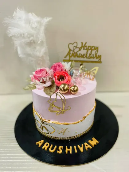 A beautiful anniversary cake with a soft pink and white design, accented with golden butterflies, flowers, and a delicate white feather.