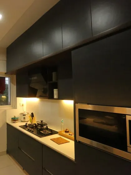 For those who prefer a bold, sophisticated look, this handleless modular kitchen in a matte black finish is a perfect choice. The warm under-cabinet lighting prevents the space from feeling too dark.