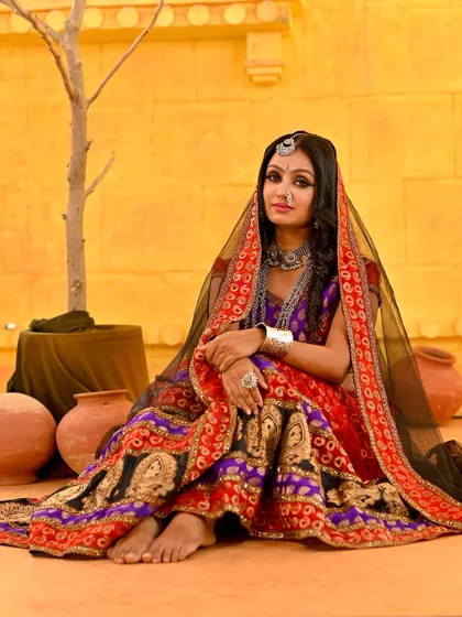 A seated portrait that showcases the full splendor of the traditional Rajasthani ghagra. The black veil adds a touch of mystery and elegance.