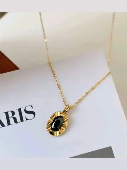 A stylish shot of the black oval stone pendant necklace resting on a magazine. This piece is guaranteed to keep its color and add elegance to your look.