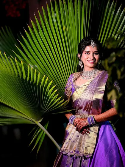 A beautiful portrait of the bride standing against a large, dramatic palm leaf, highlighting her purple and gold reception outfit.