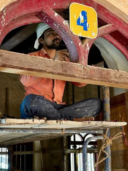 A worker perched in an arched window transom, carefully restoring the wooden frame. These high, hard-to-reach places require special care and attention to detail.