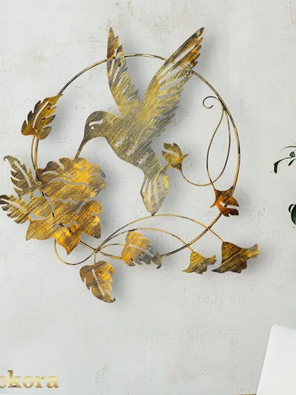 A single, beautifully detailed hummingbird crafted from metal with a rustic gold finish, captured in a moment of feeding from a flower.