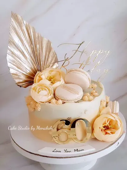 A lovely peach and gold 60th birthday cake for a mom, made completely without fondant. This elegant design is adorned with flowers, macarons, and a dried palm spear.