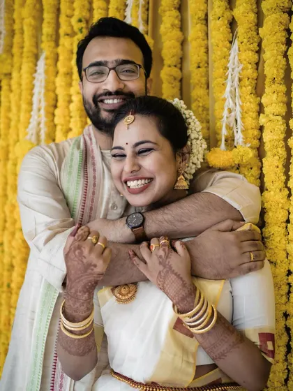 A joyful, candid portrait of a couple against a vibrant marigold backdrop. Their happy embrace and bright smiles perfectly capture the festive spirit of an Indian wedding.