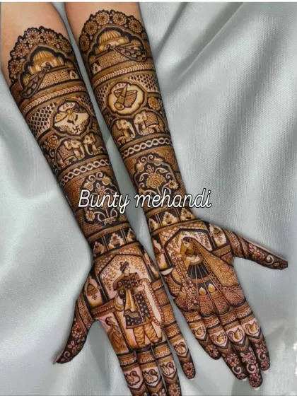 This full-arm bridal mehendi features a classic Dulha-Dulhan portrait on the palms, surrounded by traditional Rajasthani patterns and animal motifs.