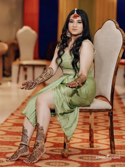 A full-length portrait of the bride seated, showcasing her complete Mehendi look and detailed henna.