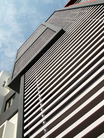 A detail of a housing project featuring brutalist-inspired design elements. The facade is dominated by strong horizontal lines created by louvers, which provide both a powerful aesthetic and functional sun shading.