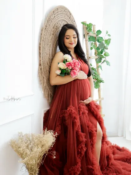 A beautiful portrait in a rustic, boho-chic setting. The mom-to-be's rich red gown and the natural textures create a warm and inviting atmosphere.