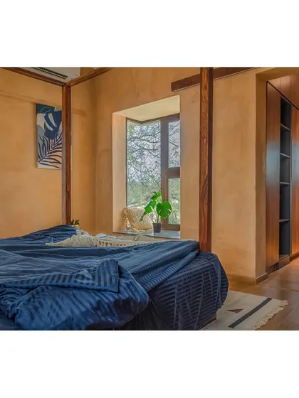 A bedroom in the villa, featuring earthy lime-washed walls and a large window with a built-in seat. The material palette creates a warm, serene, and restful atmosphere.