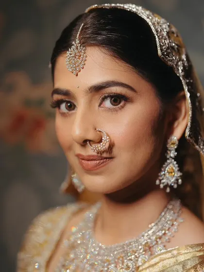 A stunning close-up of the bride, showcasing her flawless makeup and exquisite diamond jewelry. Her traditional nath and maang tikka complete the timeless bridal look.