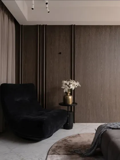 This interior detail highlights modern minimalism through disciplined design. Linear oak panels anchor the wall, while marble flooring provides a timeless base. A plush black lounge chair offers a comfortable corner for reading.