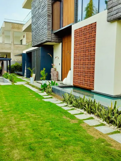 A long view of the Jaipur garden, showing the manicured lawn, stone pathway, and a striking blue sculpture that acts as a focal point.
