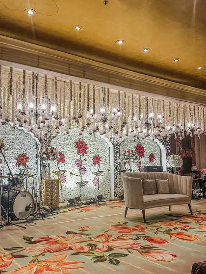 The stage for a sangeet, set up for a live band with a backdrop of floral-printed arches and a ceiling of hanging floral strings, blending performance and decor.