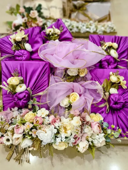 This image shows a complete set of engagement gifts wrapped using the Furoshiki technique. The consistent use of purple fabric and pastel florals creates a stunning, unified presentation.