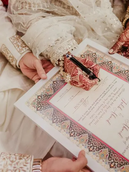 A close-up of the Nikah contract, beautifully decorated, being signed by the groom.