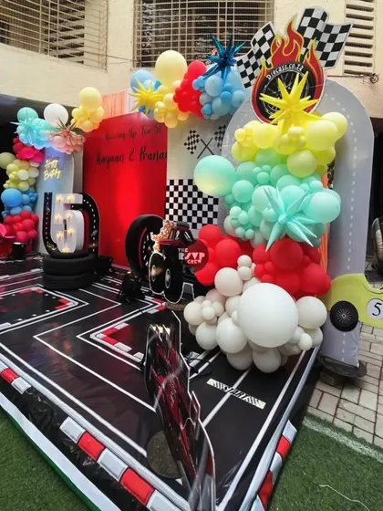 The main stage for the Hot Wheels party, featuring a custom racetrack floor, a vibrant red backdrop, and a mix of colorful and checkered balloons.