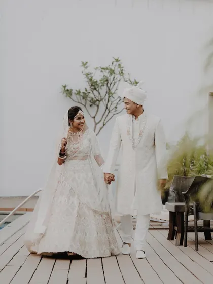 A full-length shot of the couple walking by the pool, hand-in-hand. Their coordinated white outfits look elegant and timeless.