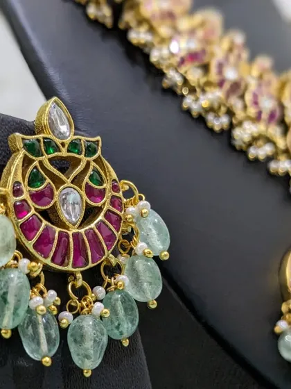 A close-up of the pink and green Jadau Chaand Baali earrings with strawberry bead drops.
