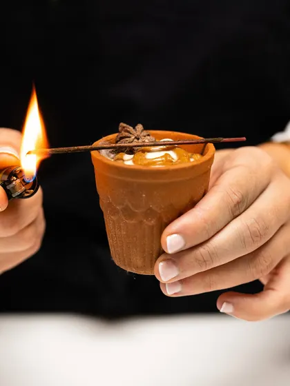 A chef lights an incense stick to add an aromatic element to a chai-spiced dessert served in a traditional kulhad, engaging all the senses.