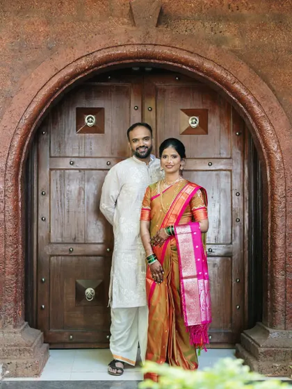 A formal portrait of the couple in front of a grand, traditional wooden door, showcasing their elegant ethnic wear and poised connection.