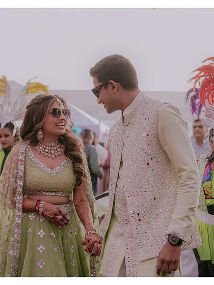 A candid shot of the couple, hand-in-hand, sharing a smile during their wedding carnival, surrounded by colorful performers.
