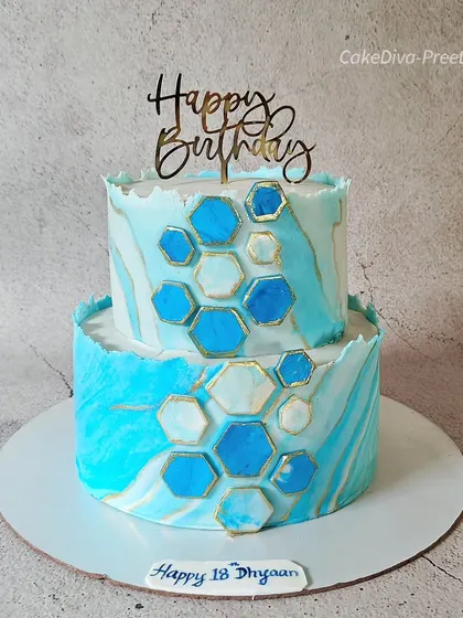 A modern two-tier cake for an 18th birthday, featuring a marbled blue fondant effect and geometric honeycomb accents. The rough edges on each tier give it a stylish, rustic look perfect for a young adult's celebration.