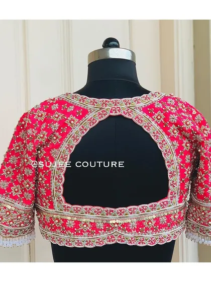 A festive and heavily embroidered back design. This pink blouse has a wide keyhole cutout, and the entire surface is covered in a dense pattern of zardozi and sequin work.