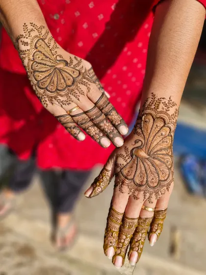 A custom design featuring a single, elegant peacock with its feathers spread across the back of the hand. The other hand has a complementary fan-like pattern.
