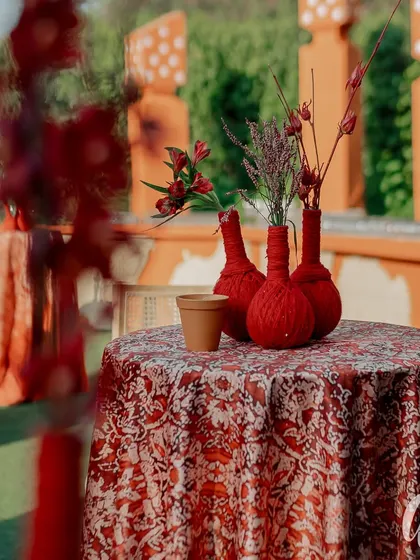 A close-up of a side table featuring custom red yarn-wrapped vases and printed linens. These small details in texture and pattern are key to building a rich, layered design.