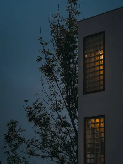 This series of images shows how the home's exterior transforms from day to night. The glass block walls, which provide privacy during the day, become luminous features in the evening, creating a warm and inviting aura.