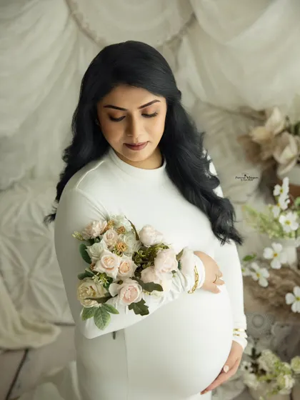 A close-up portrait of a mother-to-be in a white gown, holding a bouquet of delicate flowers. The soft textures and colors create a gentle and romantic feel.