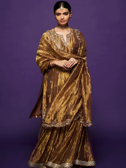 A full-length view of the metallic gold sharara set, showing its beautiful texture and the way it catches the light.