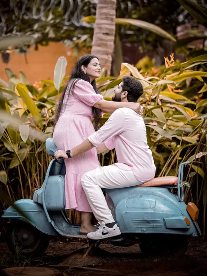 Another angle of the couple on the retro blue scooter, capturing their joyful interaction and the beautiful garden setting.