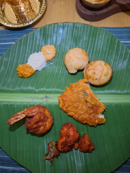 A platter of delicious South Indian appetizers, including fried prawns and paniyaram, served on a banana leaf.