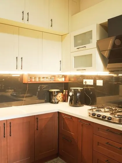 This view showcases the combination of the dark wood base cabinets and the off-white upper cabinets with frosted glass doors. The under-cabinet lighting brightens the workspace and highlights the dark backsplash.