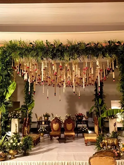 A wide view of a traditional mandap with lush greenery, hanging florals, and golden decor elements.