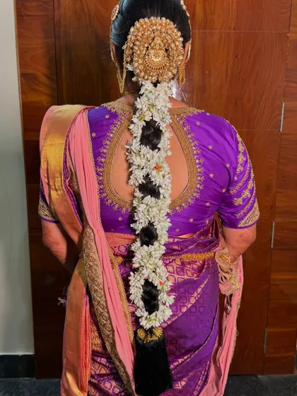 The back view of Hima's beautiful muhurtham hairstyle. The traditional braid is adorned with fresh flowers and a statement hair accessory, creating a divine look.