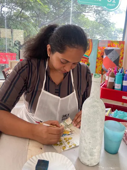 A participant carefully applies a design to a bottle during a decoupage workshop. The focus required is part of the therapeutic experience.