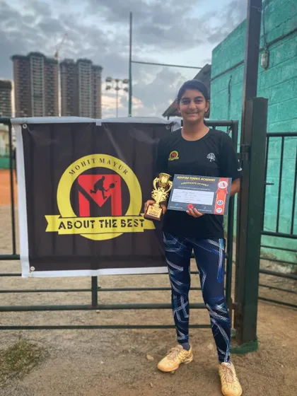Yahana posing with her winner's trophy in front of the academy banner.