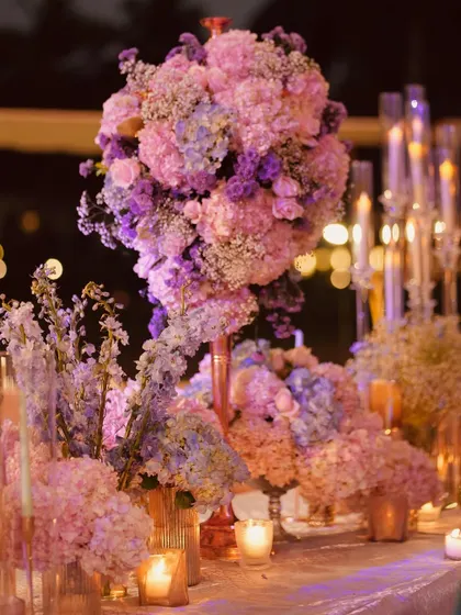 The tablescape viewed under a purple light, which enhances the lavender and blue tones in the floral arrangements. This demonstrates our ability to use lighting to completely transform the mood of a space.